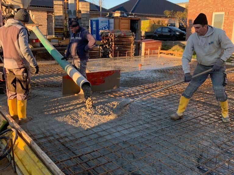 Zwei Arbeiter verteilen Beton aus dem Schlauch der Betonpumpe über der Bewehrung