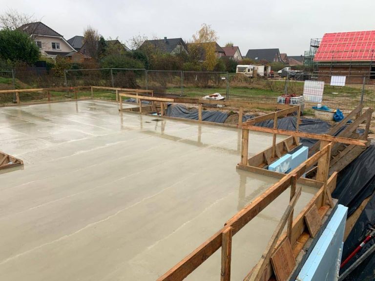 Frisch abgezogene Betonbodenplatte mit umlaufender Randschalung auf einer Baustelle