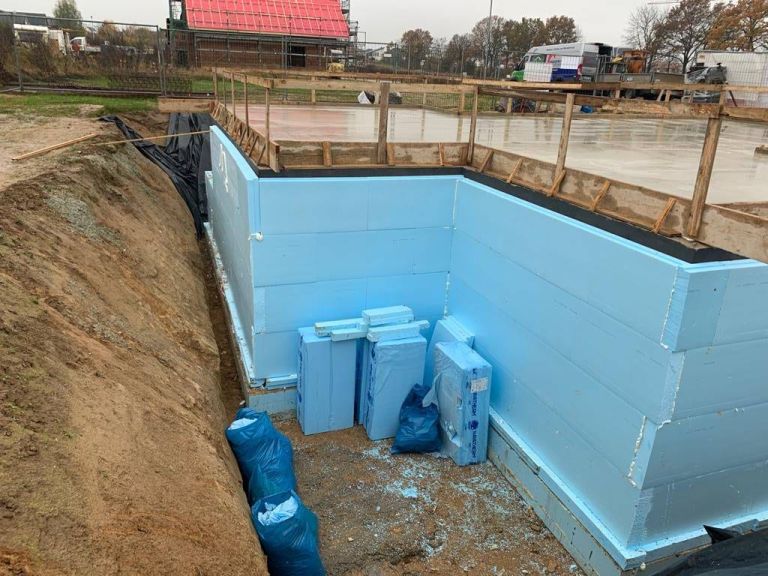 Blaue Perimeterdämmplatten an der Außenseite eines Kellers in der offenen Baugrube